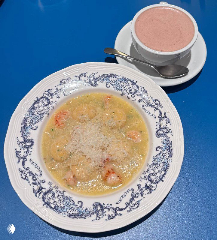 Тарелка с равиоли и креветками в кремовом соусе и кружка горячего напитка на синем столе — изображение блюда в кафе Zoe.