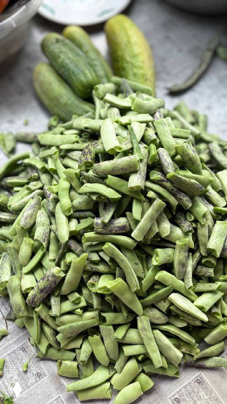 Крупный план: нарезанные и целые стручки фасоли рядом с огурцами на столе, подготовка ингредиентов для дзвов лоби в деревенской кухне.