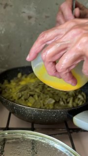 Крупный план рук, выливающих взбитые яйца в горячую сковороду с фасолью, видно масло и взаимодействие ингредиентов в процессе готовки.