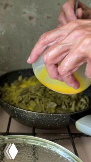 Руки вливают взбитые яйца в сковороду с жареной фасолью; видно процесс приготовления дзвов лоби на газовой плите во дворе.