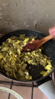 Сковорода с жарящейся фасолью и яйцом, деревянная ложка помешивает, видно текстуру и цвет готовящегося блюда на печи.