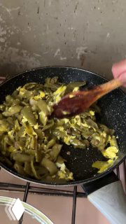 Обжаренная стручковая фасоль с кусочками яйца в сковороде, деревянная ложка перемешивает смесь — видно этап готовки блюда.