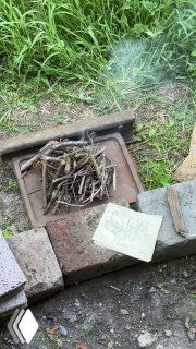 Мангал во дворе на земле, выложенный кирпичами и рельсом, вид сверху: подготовленные щепки и первые искры перед разжиганием огня в деревне.