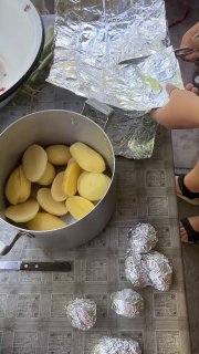 Картофель завернутый в фольгу и подготовленный для запекания в углях, несколько упакованных кусочков лежат на столе у мангала