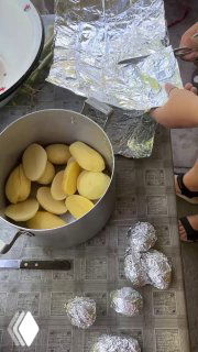 Крупный план картошки, уложенной в кастрюлю и завернутой в фольгу, а рядом несколько фольгированных «картофелин» готовы лечь в угли.