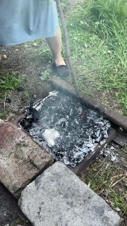 Вид на тлеющие угли в импровизированном мангале с белым пеплом и дымком, зона приготовления в саду или дворе