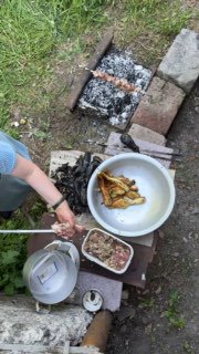 Общий вид подготовки: стол с посудой, фольгой, печёными баклажанами и ингредиентами рядом с мангалом и мисками