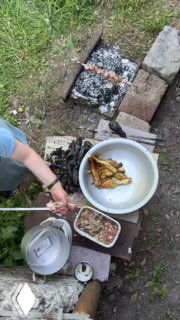 Общий план мангала с посудой и тарелками, на столе тарелка с запечёнными баклажанами и подготовленный фарш — рабочий процесс на улице.