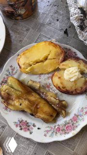 Порция готовой деревенской еды: запечённая картошка с маслом и кусочки баклажана на тарелке, поданные на столе на свежем воздухе.