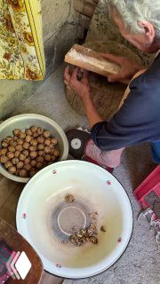 Руки и деревянная доска: процесс колки грецких орехов в домашней обстановке, миска с целыми орехами и скорлупой рядом.