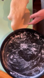 Раскатывают тесто на рабочей поверхности рядом с посыпанной мукой круглой формой для выпечки, подготовка основы.
