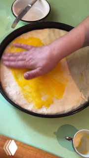 Смазка верхнего слоя теста чем-то желтоватым (вероятно желток) перед запеканием; руки разравнивают поверхность.