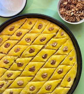 Готовые пирожные с ромбовидной нарезкой и половинками грецкого ореха сверху в круглой форме, до полива сиропом.