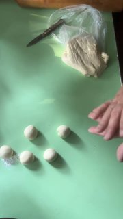 Руки готовят тесто для хинкали на зелёной поверхности: кусок теста, нож и несколько аккуратно скатанных шариков теста готовы к раскатыванию и лепке.