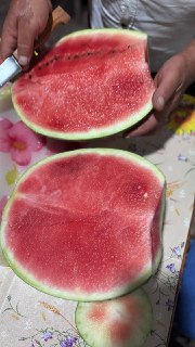 Разрезанный арбуз с ярко‑красной сочной мякотью и семенами на столе; кадр показывает плотную структуру фрукта, нож и цветную скатерть под ними.