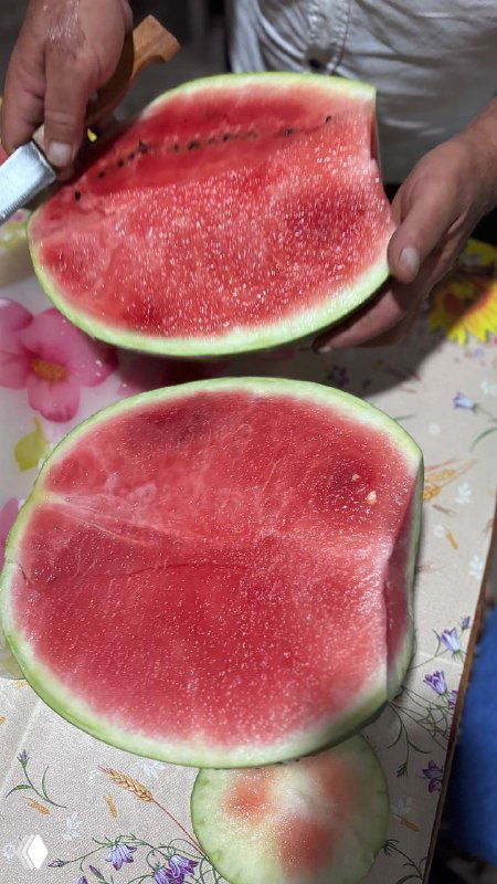 Разрезанный хрустящий арбуз: крупный план двух половинок с яркой красной мякотью и крупными семенами на столе в летней обстановке.