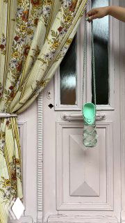 Самодельный вязаный чехол для бутылки, подвешенный у дверного проёма — простая рукодельная деталь быта и домашнего уюта в деревне.