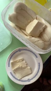 Контейнер с белым домашним сыром и кусочки на тарелке; кадр показывает текстуру сыра, кухонную посуду и близкую сцену деревенской кухни с деталями.