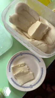 Контейнер с домашним белым сыром и куски сыра на тарелке рядом — простая молочная еда, похожая на творог или домашний сыр.