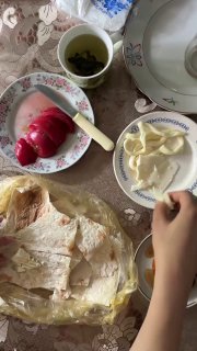 Лаваш, разложенные кусочки сыра и помидор на столе, рука в кадре; сцена простой деревенской трапезы с посудой, упаковкой и текстурами продуктов.
