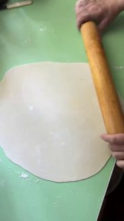 Руки раскатывают пласт теста скалкой на столе — кадр процесса приготовления татар бераги, без лиц, только руки и тесто.