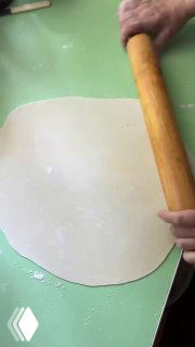 Руки раскатывают тонкий лист теста на зелёной рабочей поверхности — начало приготовления татар бераги в домашней кухне, кадр процесса.