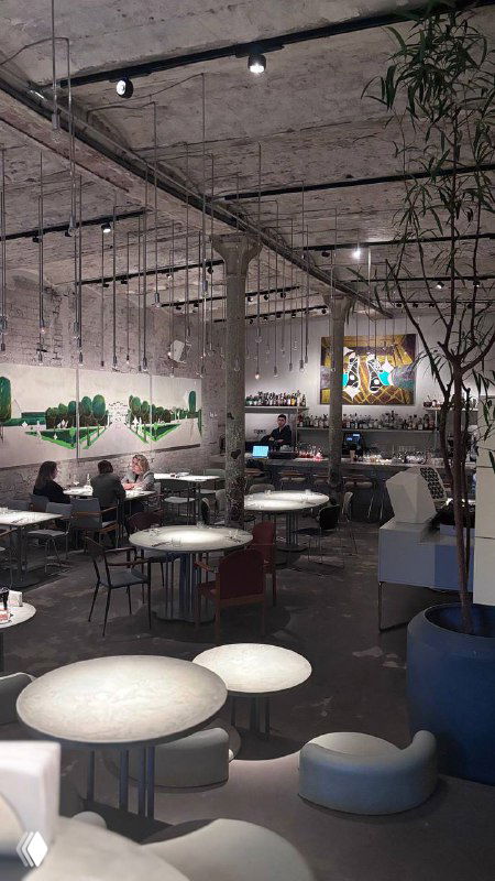 Интерьер ресторана Soma: широкий зал с индустриальным потолком, столами, стульями и картинами на стенах в мягком свете