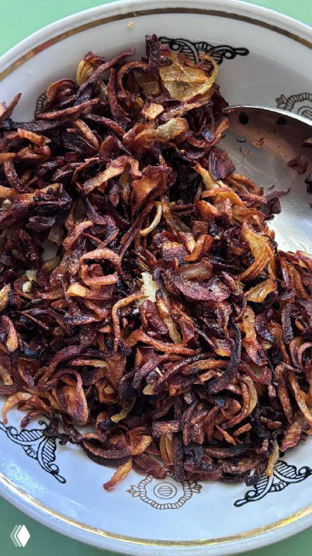 Золотисто‑коричневый жареный лук горкой на тарелке — хрустящая ароматная начинка/добавка, которая покрывает татар бераги при подаче.