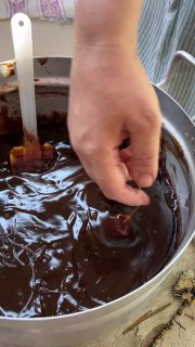 Рука опускает нанизанную нить с орехами в густую тёмную виноградную пасту в большой ёмкости — обмакивание чурчхелы.