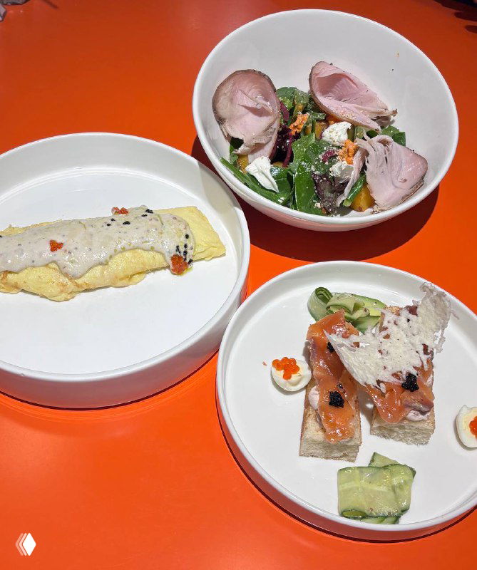 Три блюда на белых тарелках на оранжевом столе: гравлакс с перепелиным яйцом и икрой, пармезановый чипс и салат — праздничная сервировка в Скворце