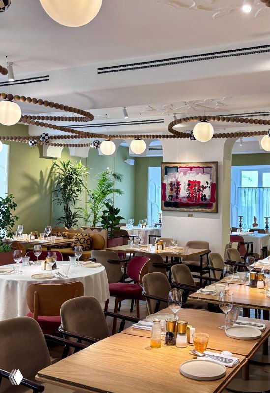 Интерьер ресторана Mouflon: светлый зал с круглыми лампами, зелёными акцентами, расставленными столами и сервировкой, уютная обстановка.