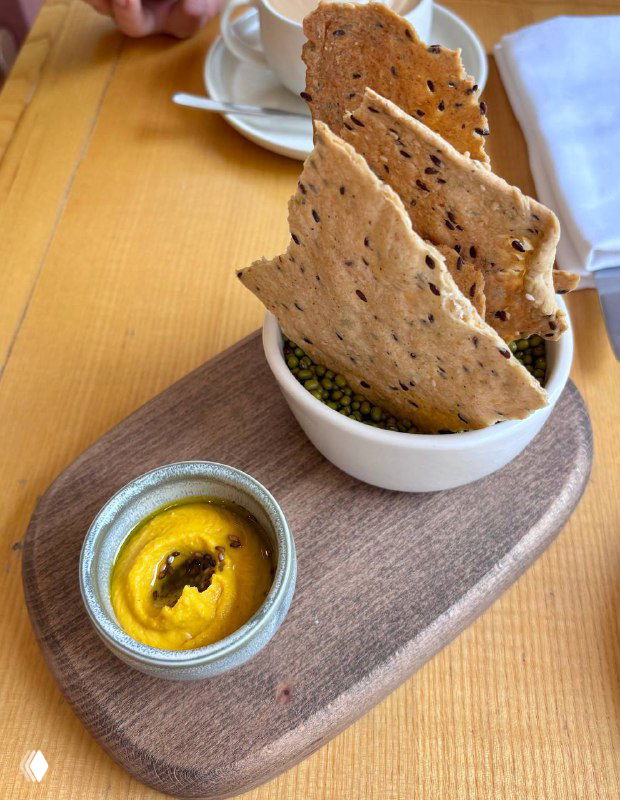 Подача мезе: хрустящие крекеры на деревянной доске и мисочка с горчично-жёлтой пастой, аккуратная сервировка на столе ресторана.