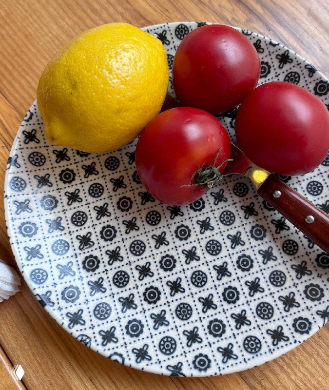 Тарелка с большим лимоном и тремя яркими помидорами-черри на узорчатой тарелке; простая летняя композиция на столе ресторана.