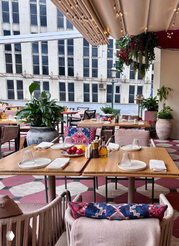 Терасса или зона у окна ресторана Mouflon: столики с сервировкой, подушки на стульях и вид на город — лёгкая летняя атмосфера.