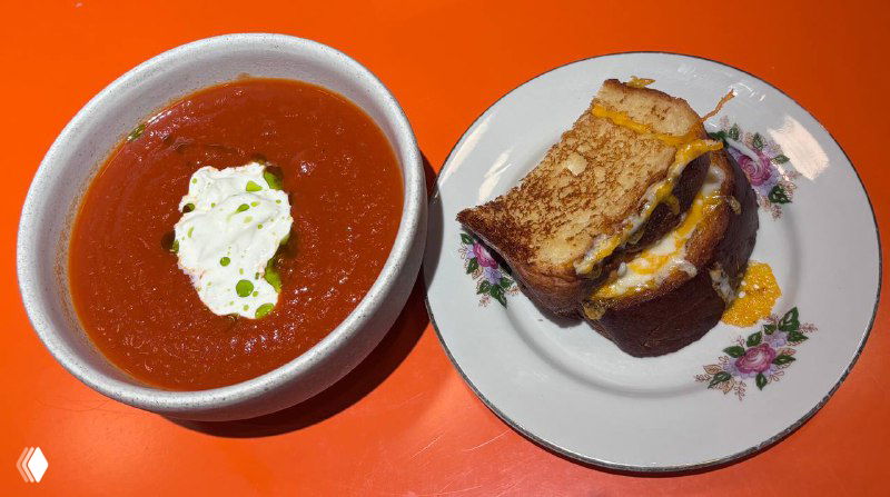 Томатный суп в белой миске рядом с бриошью и сэндвичем на тарелке — подача домашнего супа со страчетеллой в кафе Скворец