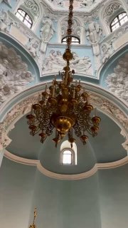 Хрустальная или бронзовая люстра в центральном зале церкви Дубровицы: подвесной светильник на фоне купольного свода и окна.