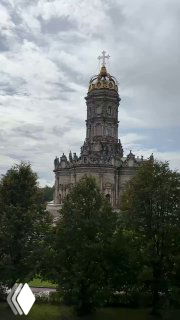 Вид со стороны парка на силуэт Знаменской церкви: купол, башенка и зеленая кромка деревьев под облачным небом.