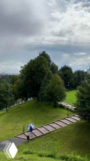 Тропинка в липовом парке усадьбы Дубровицы: ступени, зеленые деревья и человек с зонтом, отражение небольших луж на дорожке.