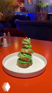 Небольшая новогодняя елочка из профитролей с зелёной помадкой на белой тарелке — десертная акция в декабрьском меню Скворца