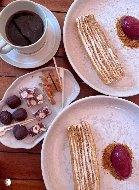 Крупный кадр тарелки с десертом: текстурная крошка, сироп и ягодный сорбет — светлая сервировка и чашка кофе рядом.