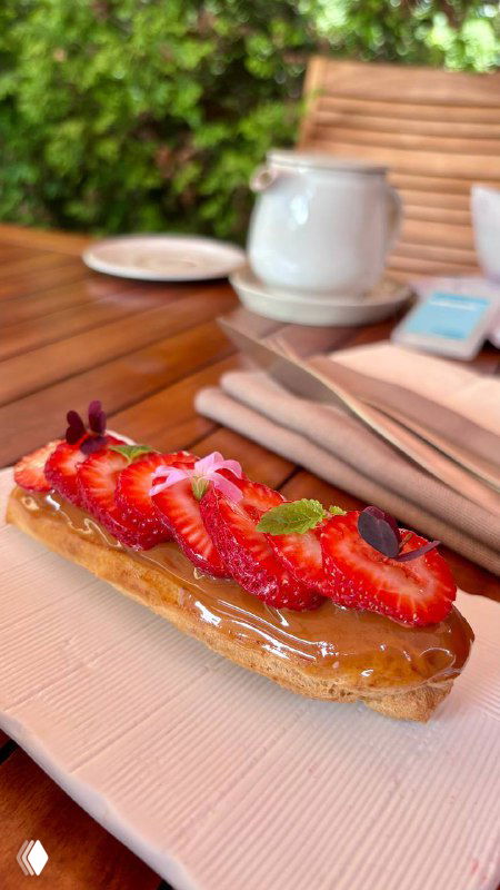 Длинный эклер с ягодами на тарелке на фоне столовой посуды — яркий ягодный декор и тонкая глазурь на десерте.