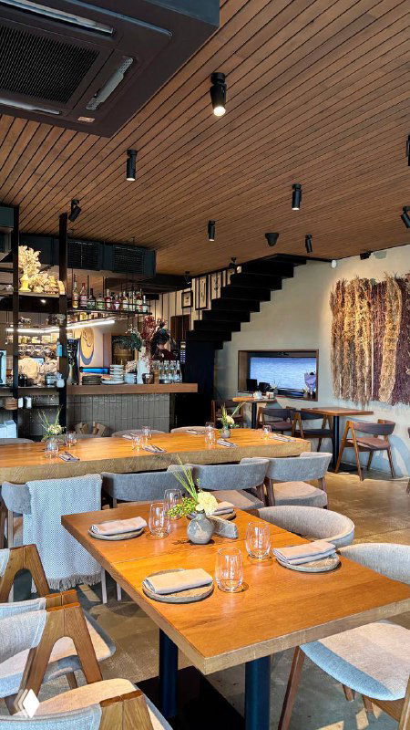 Интерьер ENO Bistro: столы, деревянные панели, тёплое освещение и уютная современная обстановка ресторана с видом на зал.