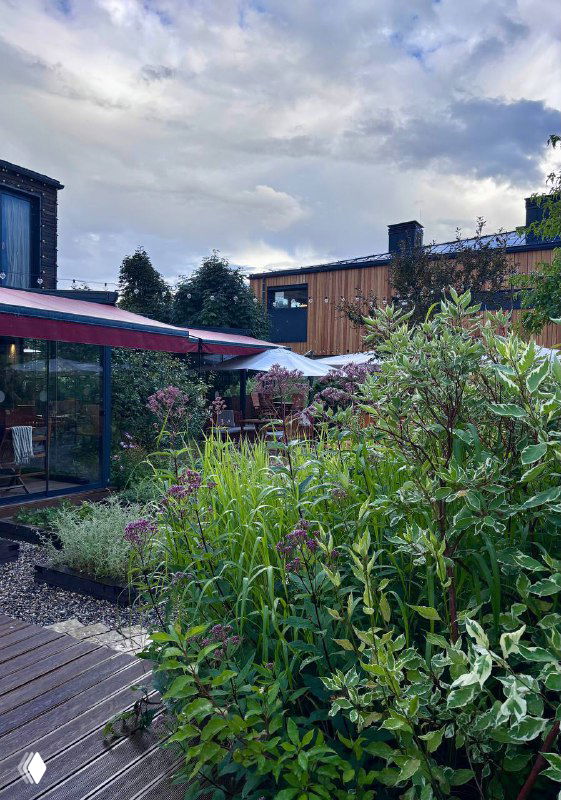 Открытая веранда и густые зелёные кусты вокруг столов на свежем воздухе — место для ужина среди растений и спокойной атмосферы.