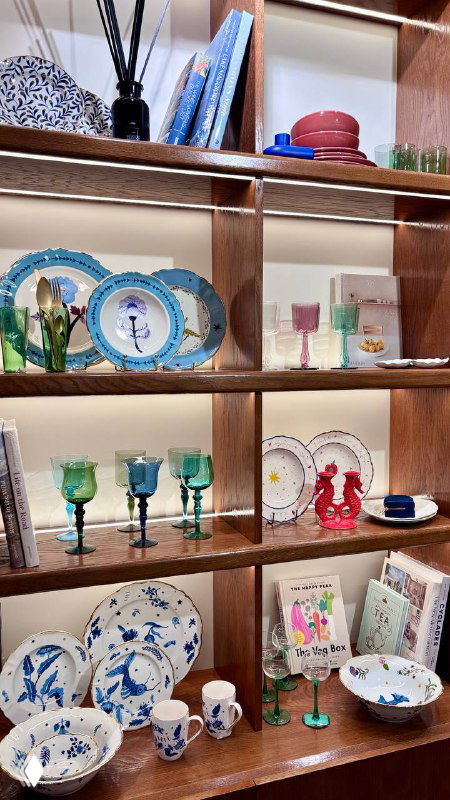 Полка с декоративной посудой и бокалами на витрине кофейни-магазина Nuself: тарелки, бокалы и мелкие предметы декора, эстетичный магазинный стеллаж.