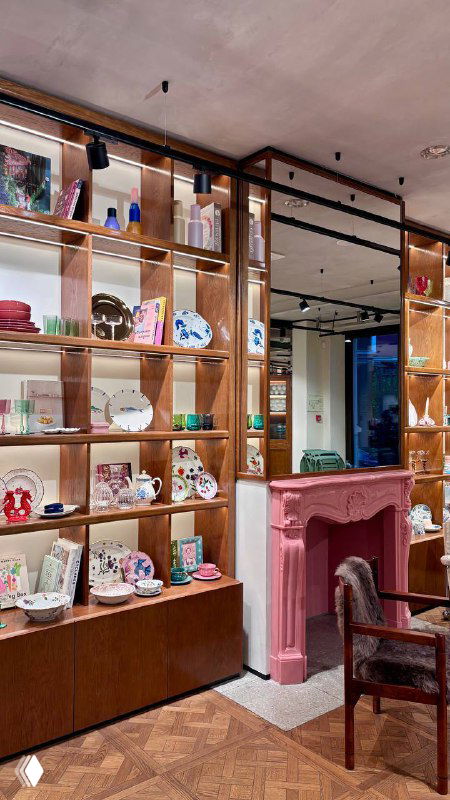 Интерьер кофейни при магазине Nuself: полки с посудой, розовый камин и кресло в уютной зоне для сидения, пастельная уютная атмосфера.