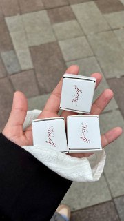 Рука держит небольшие коробочки с логотипом Nuself; вид на подарочную упаковку или конфетки крупным планом на улице.