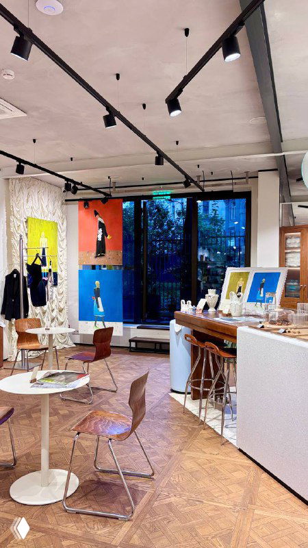 Общий вид интерьера кофейни при магазине Nuself: столы, стулья и настенные картины, просторное помещение с дизайнерской отделкой и теплыми цветами.