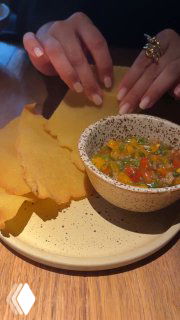 Тарелка с хрустящими чипсами и миской соуса, на переднем плане рука гостя; тёплое приглушённое освещение ресторана Tacobar