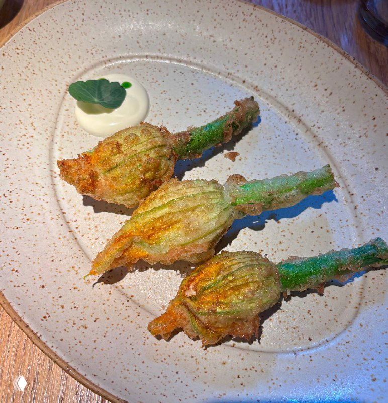 Четыре цветка цукини в кляре на белой тарелке с ложечкой соуса; золотистая хрустящая корочка и зелёные хвостики