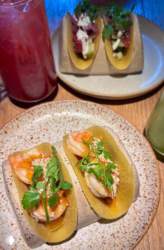 Два тако с креветками и яркими добавками рядом с напитками; аккуратная подача в стиле Tacobar на деревянном столе